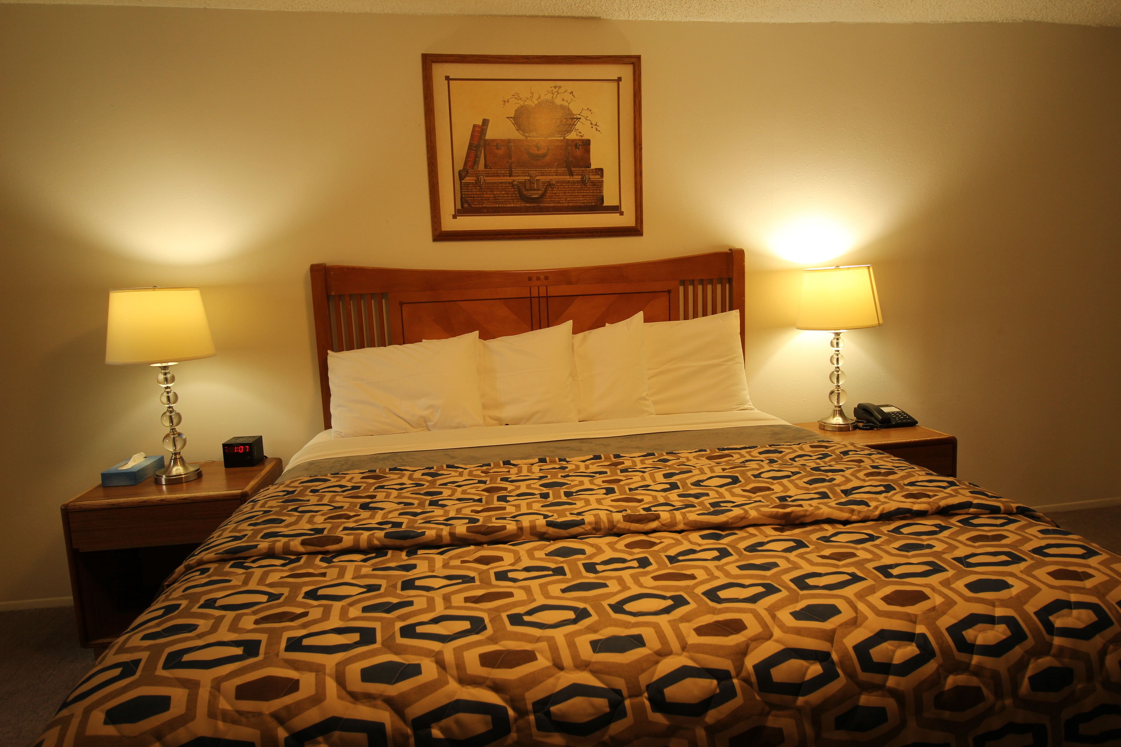A hotel room with a bed, two bedside lamps, a nightstand with a phone, and a framed picture on the wall.