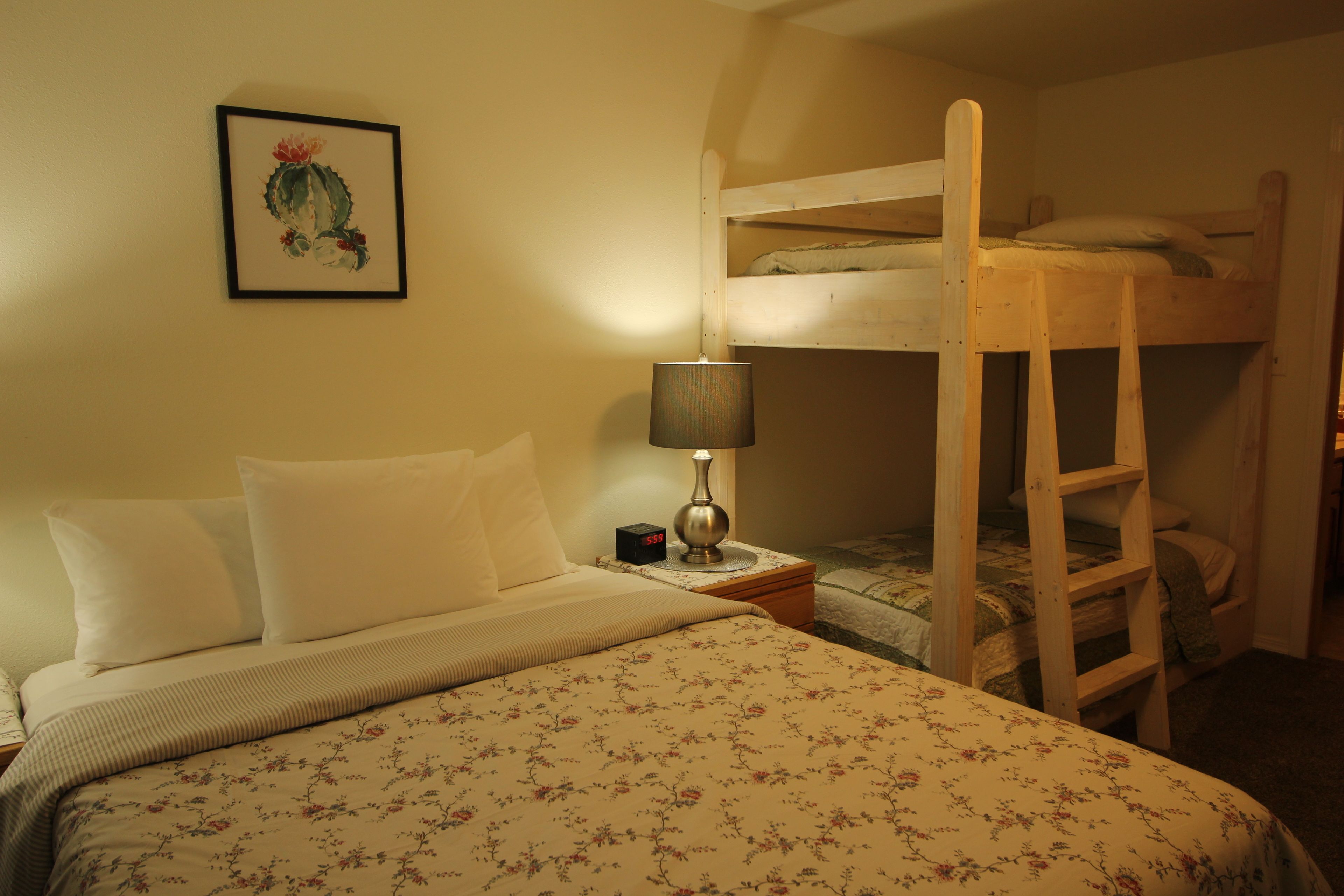 A bunk bed room with a single bed, a nightstand with a lamp, and a framed picture on the wall.