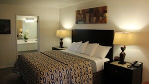 Une chambre d’hôtel avec un grand lit, deux tables de chevet avec des lampes, une petite table avec un téléphone, un tableau au mur et un miroir agrémenté d’un vase de fleurs.