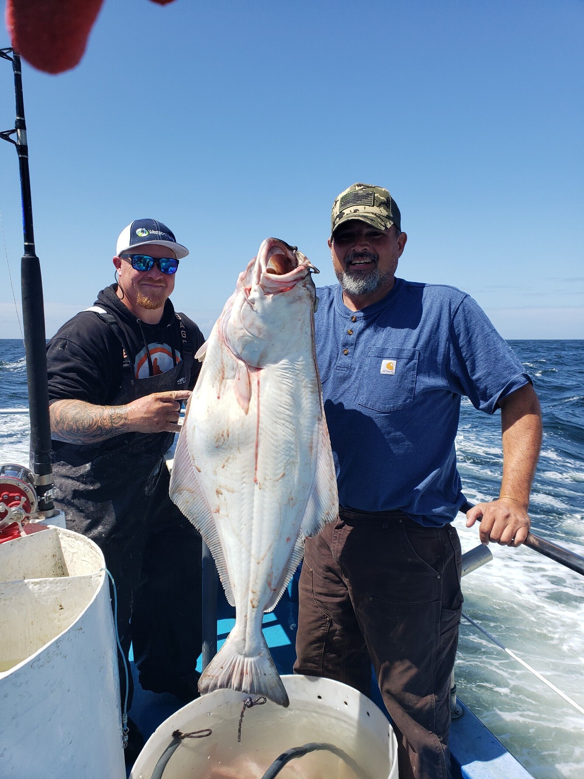 Two individuals on a boat holding a large fish.
