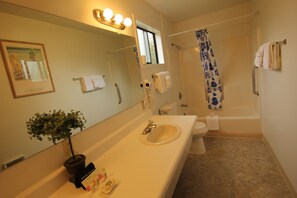 A bathroom with a sink, mirror, potted plant, and a shower with a blue patterned curtain.