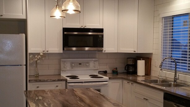 A modern kitchen with white cabinetry, a central island, stainless steel appliances, and pendant lighting. - New Construction Coach House, 10 Minute Walk to Downtown and Ferry Spotless (Nanaimo)