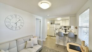 Ein modernes Wohnzimmer mit einer Couch, einer Uhr und einer Küche im Hintergrund.