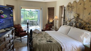 Habitación de hotel con cama, televisor mostrando una carrera de NASCAR, balcón con mobiliario exterior y ventilador de techo.