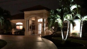 Una entrada bien iluminada con un camino de acceso curvo que lleva a un edificio con puerta de cristal y el número '1418' a la vista.
