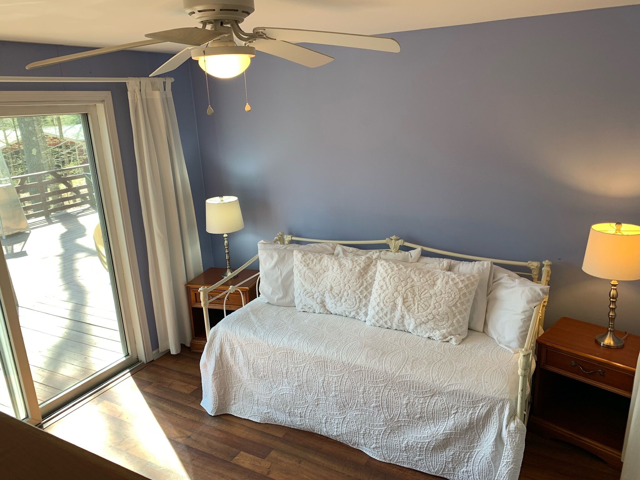 A bedroom with a bed, two bedside tables, a ceiling fan, and a view through a sliding glass door.