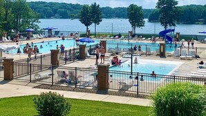 A large outdoor swimming pool with multiple lanes, surrounded by lounge chairs and umbrellas, with a lake and trees in the background. - Treasure Lake Vacation Rental (Sleeps 16!) (Du Boise)