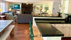 A modern living room with a stone fireplace, a flat-screen TV, a dining area with a long table, and a kitchen with white cabinets and a black countertop. - Treasure Lake Vacation Rental (Sleeps 16!) (Du Boise)