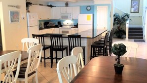 A modern kitchen with white cabinets, a central island, and a dining area with a wooden table and white chairs.