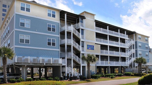A multi-story hotel with balconies, a covered walkway, and a parking area.