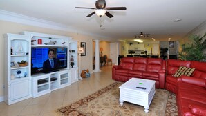 A living room with a television, red leather sofa, white entertainment unit, and a ceiling fan.