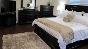 A bedroom with a large bed, a dresser, a TV, and a mirror.