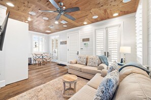 A spacious living room with a wooden ceiling, a beige sofa, and a dining area with wooden chairs.