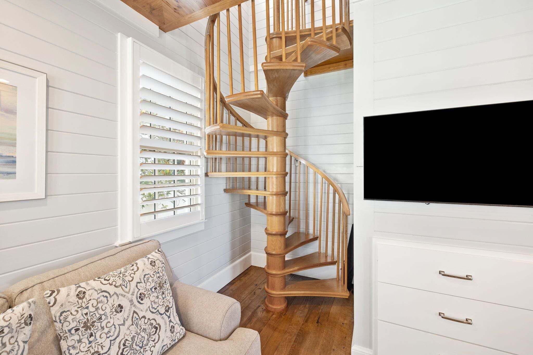 A spiral staircase in a room with white walls and wooden flooring.