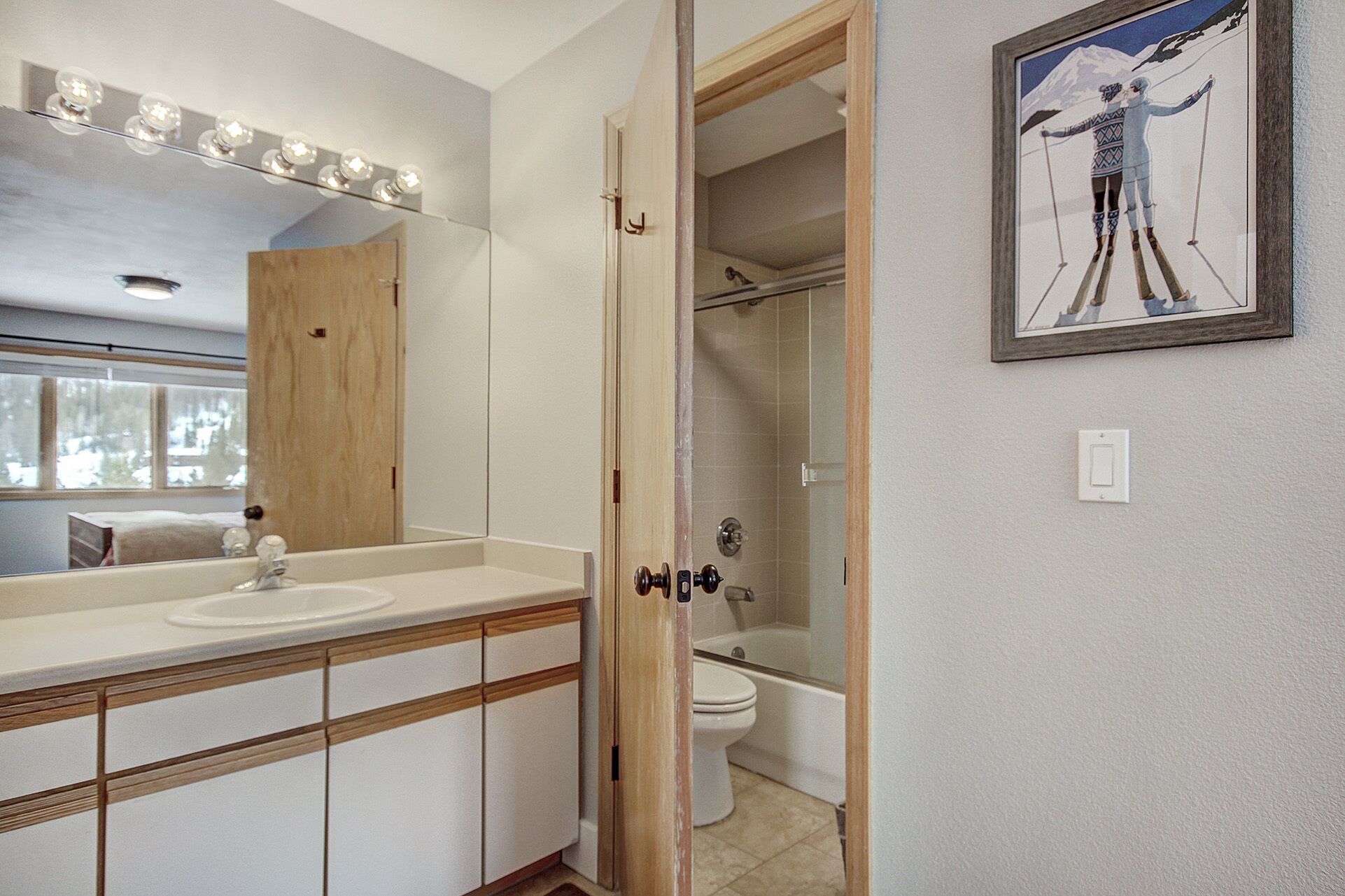 A bathroom with a vanity, mirror, and a framed picture of a skier.