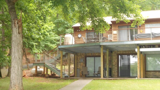 Un bâtiment à deux étages doté d’un espace extérieur couvert, d’un escalier et d’un grand arbre au premier plan.