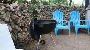 Ein schwarzer Grill mit einem Metallständer, zwei blaue Adirondack-Stühle und eine Steinmauer im Hintergrund.