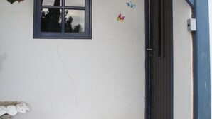 Ein Hauseingang mit blauer Fußmatte, ein kleiner Garten mit Steinen und Pflanzen, ein Fenster mit Aussicht und eine Tür mit blauem Rahmen.