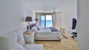 A hotel room with a bed, a desk, a TV, and a view of the sea. - Beach Front Villa in cupecoy (Lowlands)