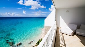 A balcony with a view of the ocean, a white railing, and two lounge chairs. - Beach Front Villa in cupecoy (Lowlands)