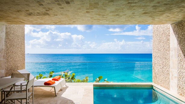 A pool area with a view of the ocean, a table with chairs, and a bench with orange cushions. - Beach Front Villa in cupecoy (Lowlands)