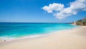 A beach with clear turquoise water, a sandy shore, and a building on the right. - Beach Front Villa in cupecoy (Lowlands)