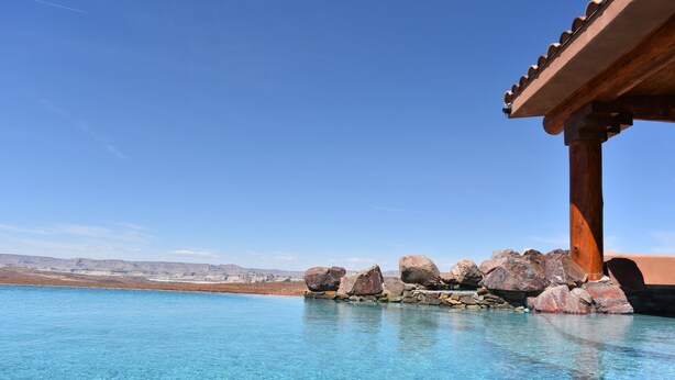Une piscine aux eaux d’un bleu limpide, agrémentée de rochers et d’une pergola en bois.