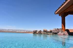 Una piscina azul cristalina con rocas y una pérgola de madera.
