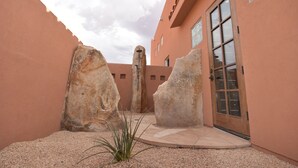 Une cour avec de gros rochers, une porte et un bâtiment dont la façade est recouverte d’enduit.