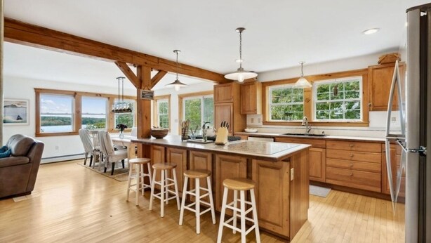 Una cocina amplia con armarios de madera, una isla grande con taburetes y ventanas que ofrecen vistas al exterior.