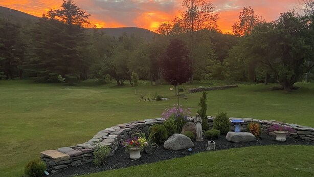 A landscaped garden with a stone border, a statue, and a variety of plants. - Windham/Hunter All-season French Country Farmhouse-Moments Away from Hayfield. (Maplecrest)