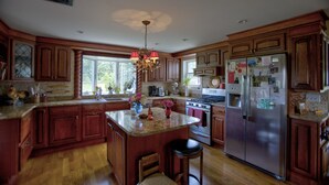 A spacious kitchen with wooden cabinets, a central island, a stainless steel refrigerator, and a chandelier. - Windham/Hunter All-season French Country Farmhouse-Moments Away from Hayfield. (Maplecrest)