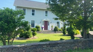 A two-story house with a stone wall in front, a red door, and a well-maintained lawn. - Windham/Hunter All-season French Country Farmhouse-Moments Away from Hayfield. (Maplecrest)