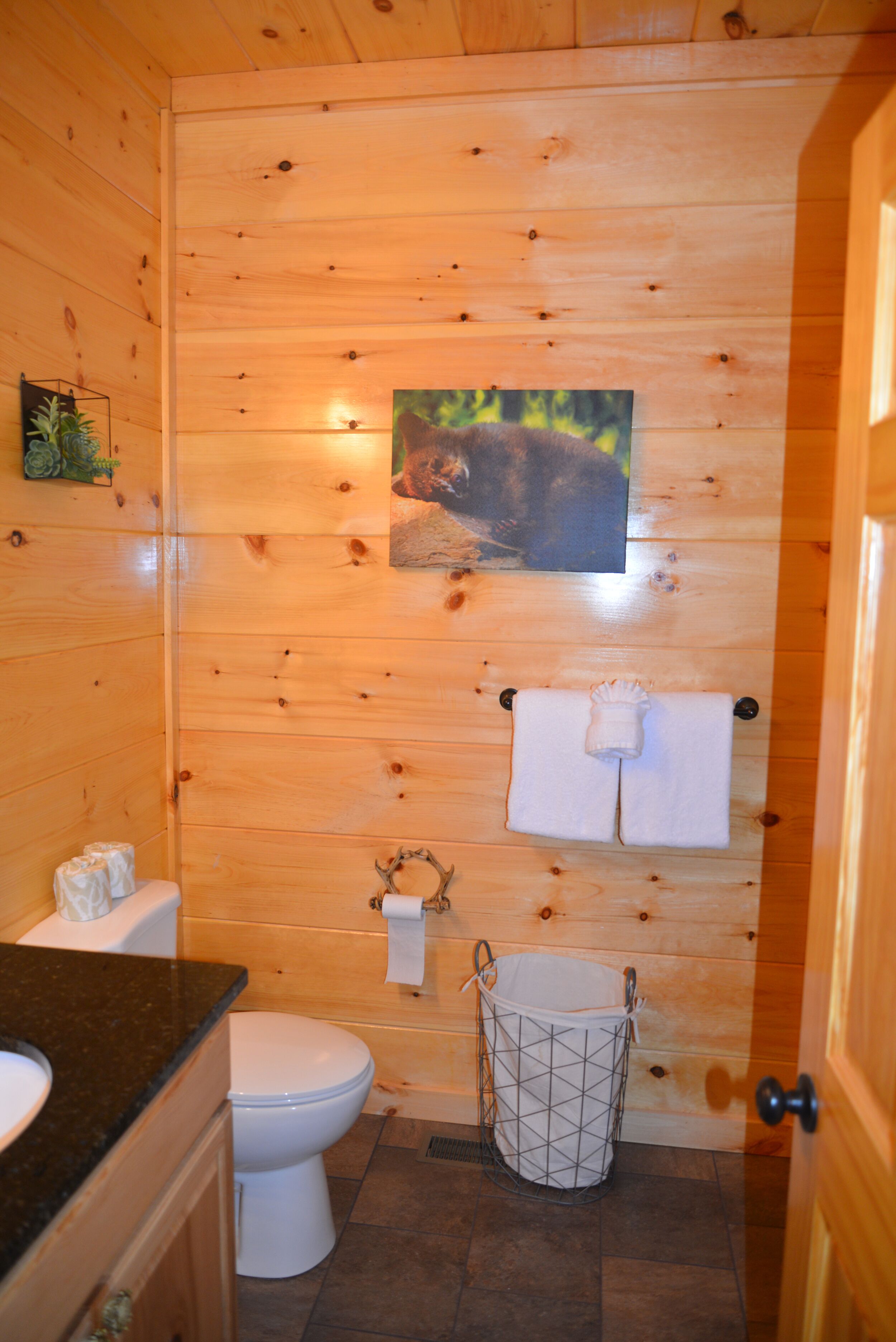 Un baño con paneles de madera, un inodoro, un lavamanos y un perchero con dos toallas.