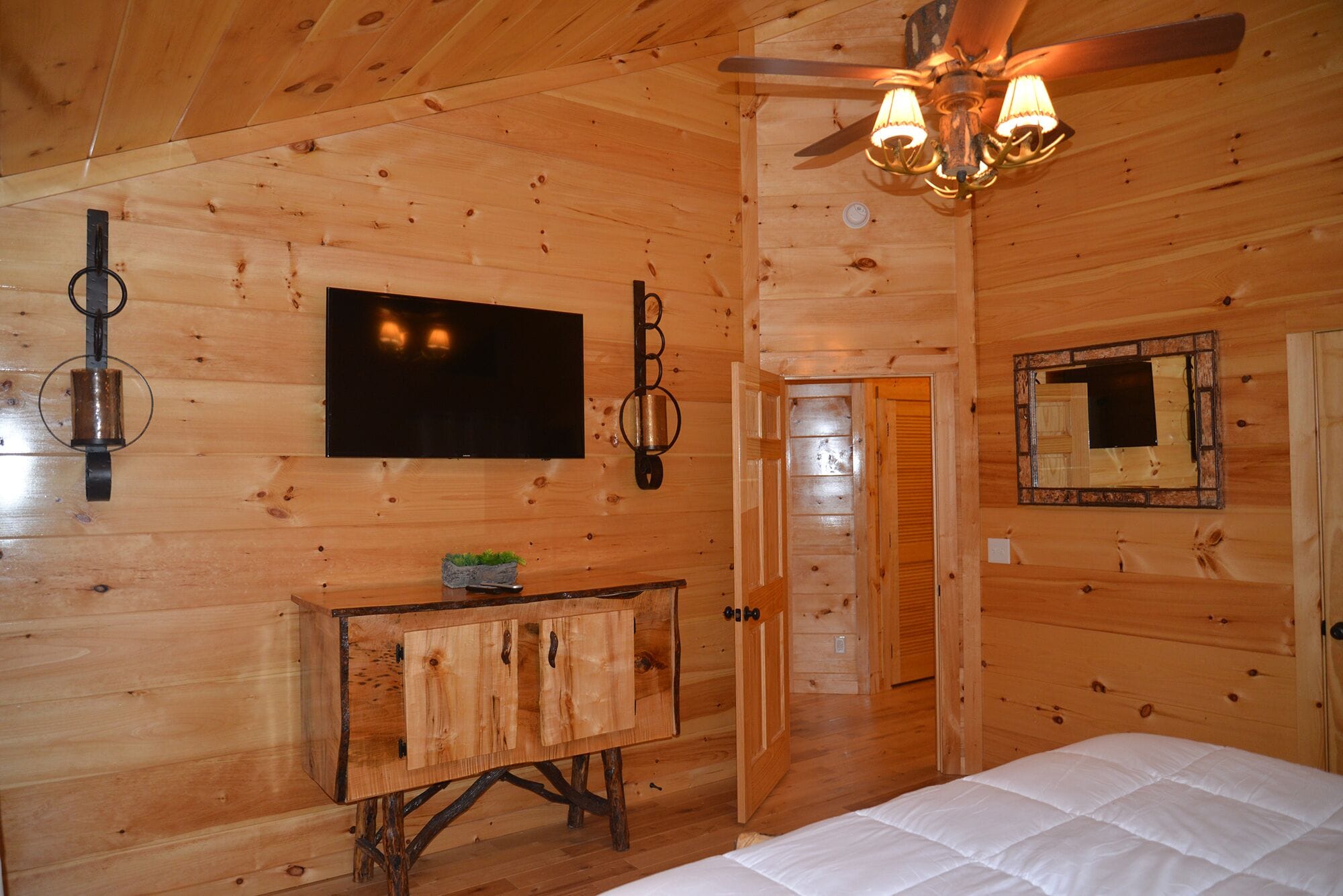 A wooden cabin room with a bed, a wooden cabinet, a television, and a ceiling fan.