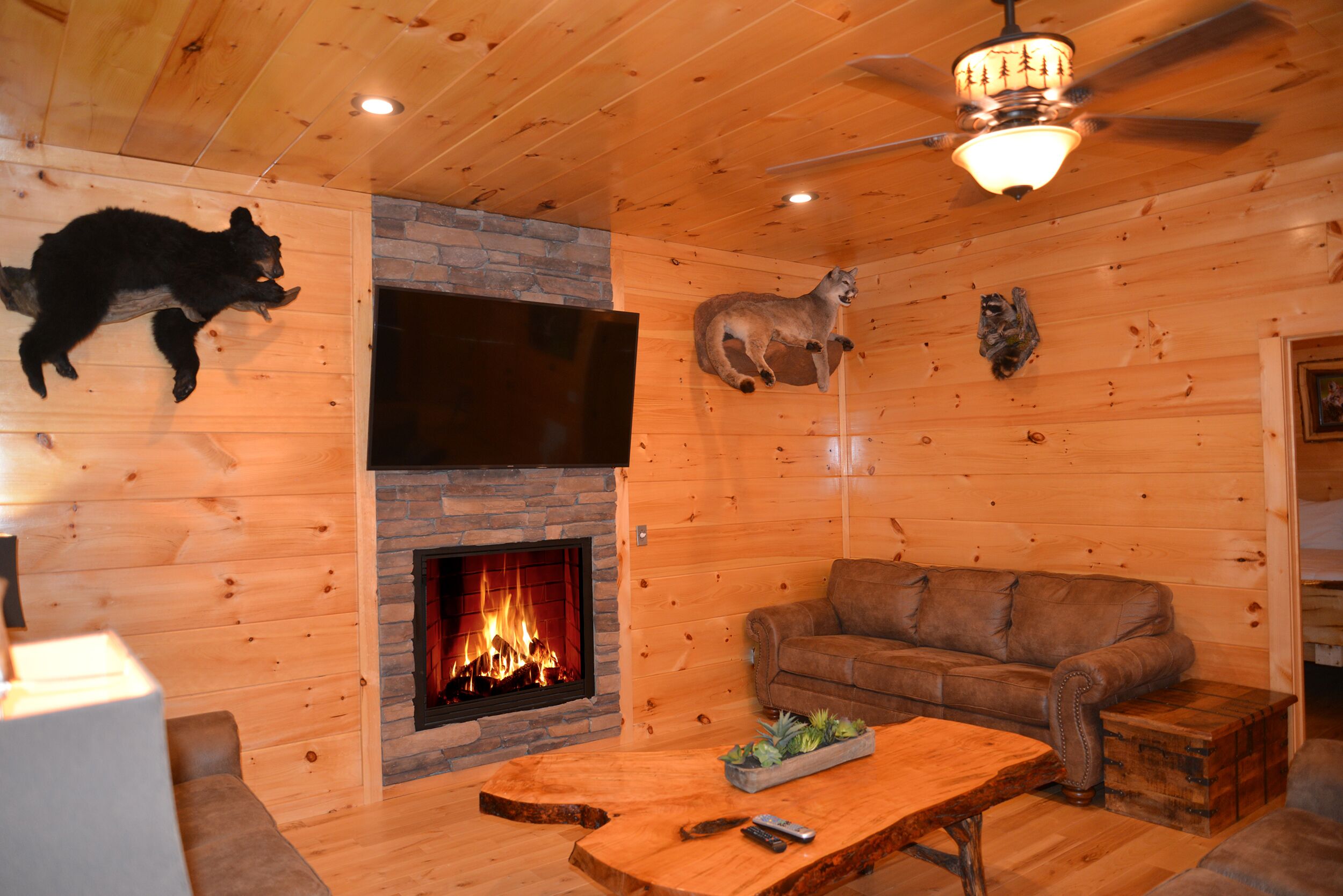 L’intérieur chaleureux d’un chalet avec une cheminée, des murs en bois, un canapé en cuir et des têtes d’animaux empaillées accrochées au mur.