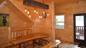 Un intérieur en bois avec une grande table à manger, des luminaires suspendus et une fenêtre offrant une vue agréable.