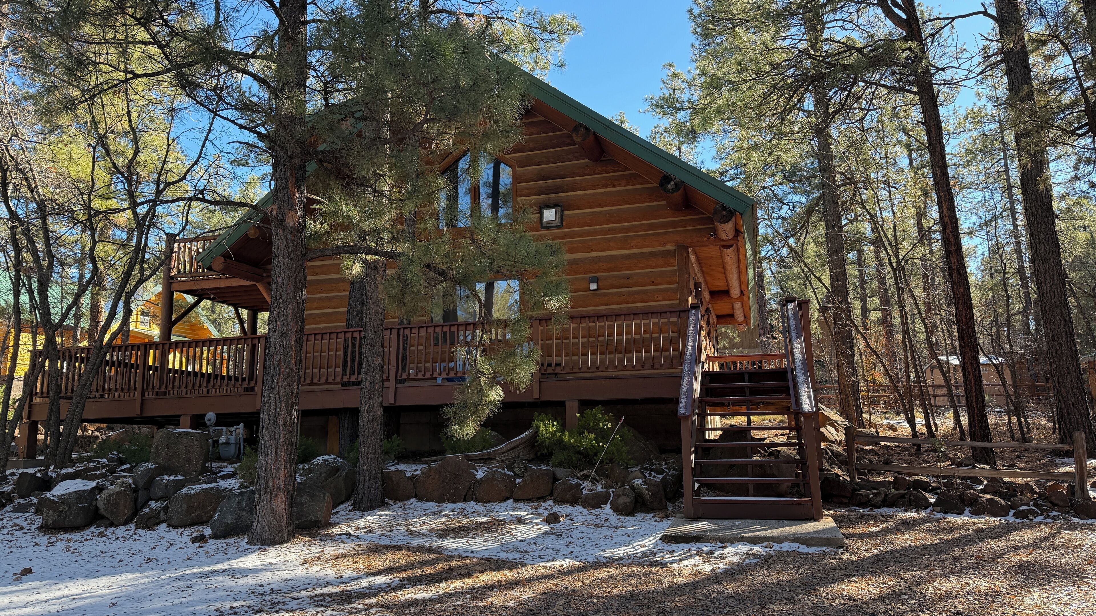 Une cabane en rondins dotée d’un balcon, entourée d’arbres et de rochers.