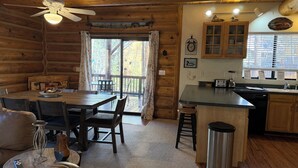 Interior acogedor de una cabaña con comedor, cocina y un amplio ventanal.