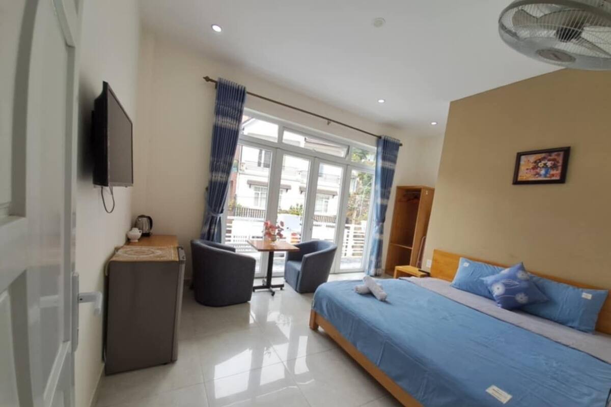 Habitación de hotel con cama, escritorio, silla, televisión y ventana con cortinas.