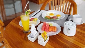 A dining table set with breakfast items including eggs, toast, and fruit, with a view of a bedroom in the background. - Paraiso Cottage Ubud (Ubud)