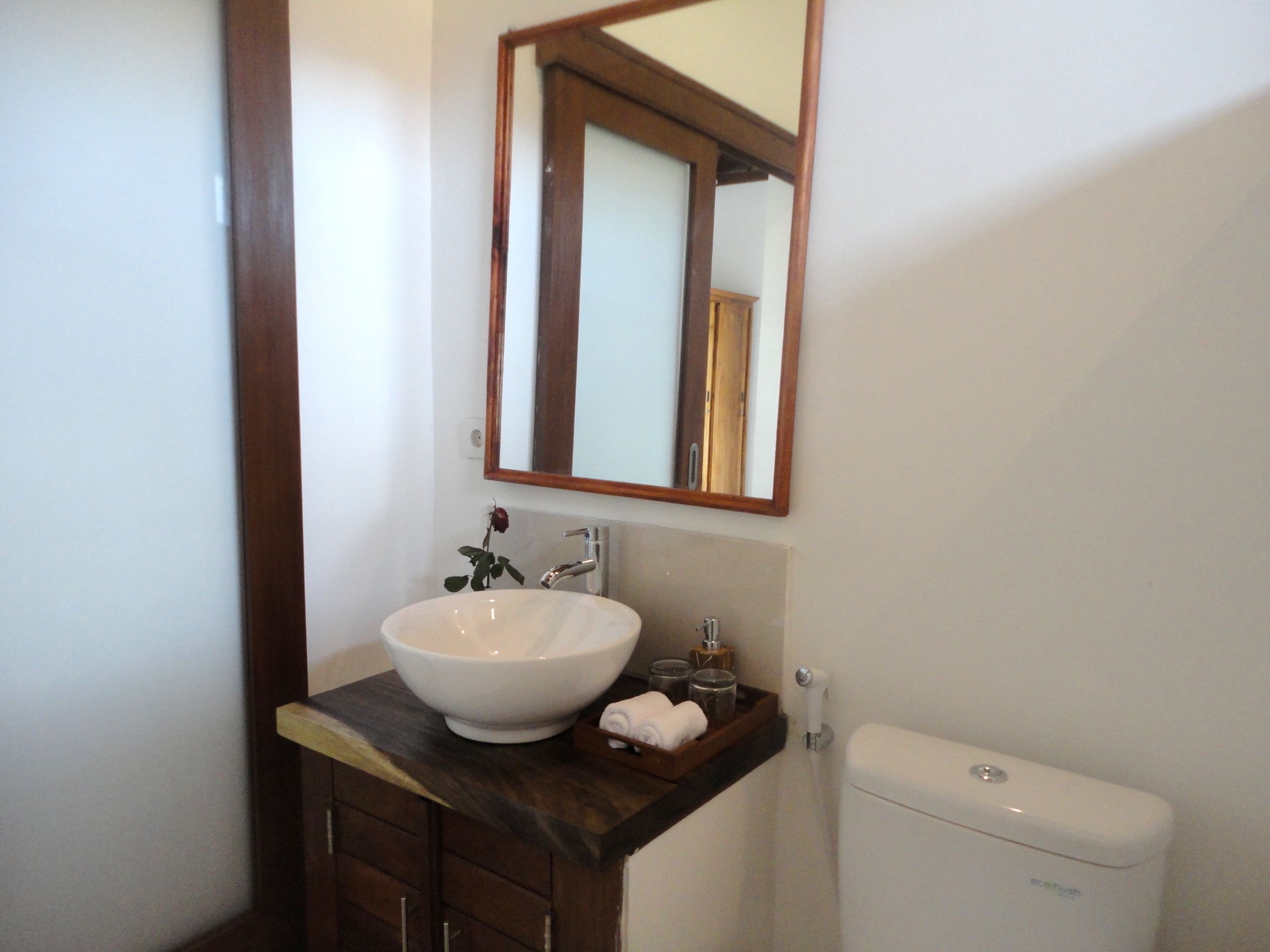 Une salle de bain avec un lavabo blanc, un meuble en bois, un miroir et des toilettes blanches.