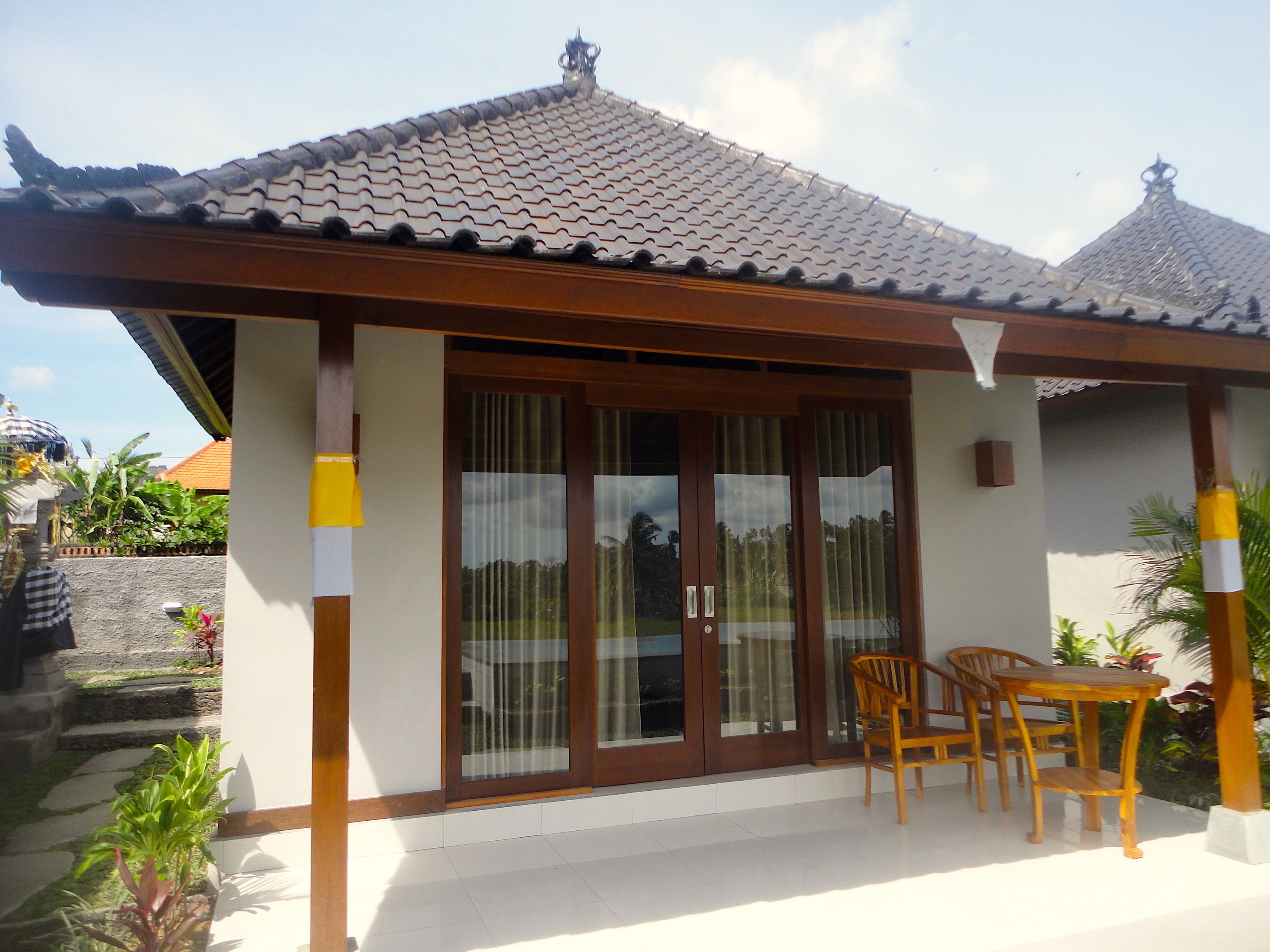 A traditional-style building with a tiled roof, large glass doors, and a small patio area with wooden furniture.