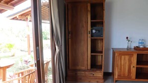 A wooden cabinet with a built-in radio, a small table with a vase and bottles, and a chair by a sliding glass door. - Paraiso Cottage Ubud (Ubud)