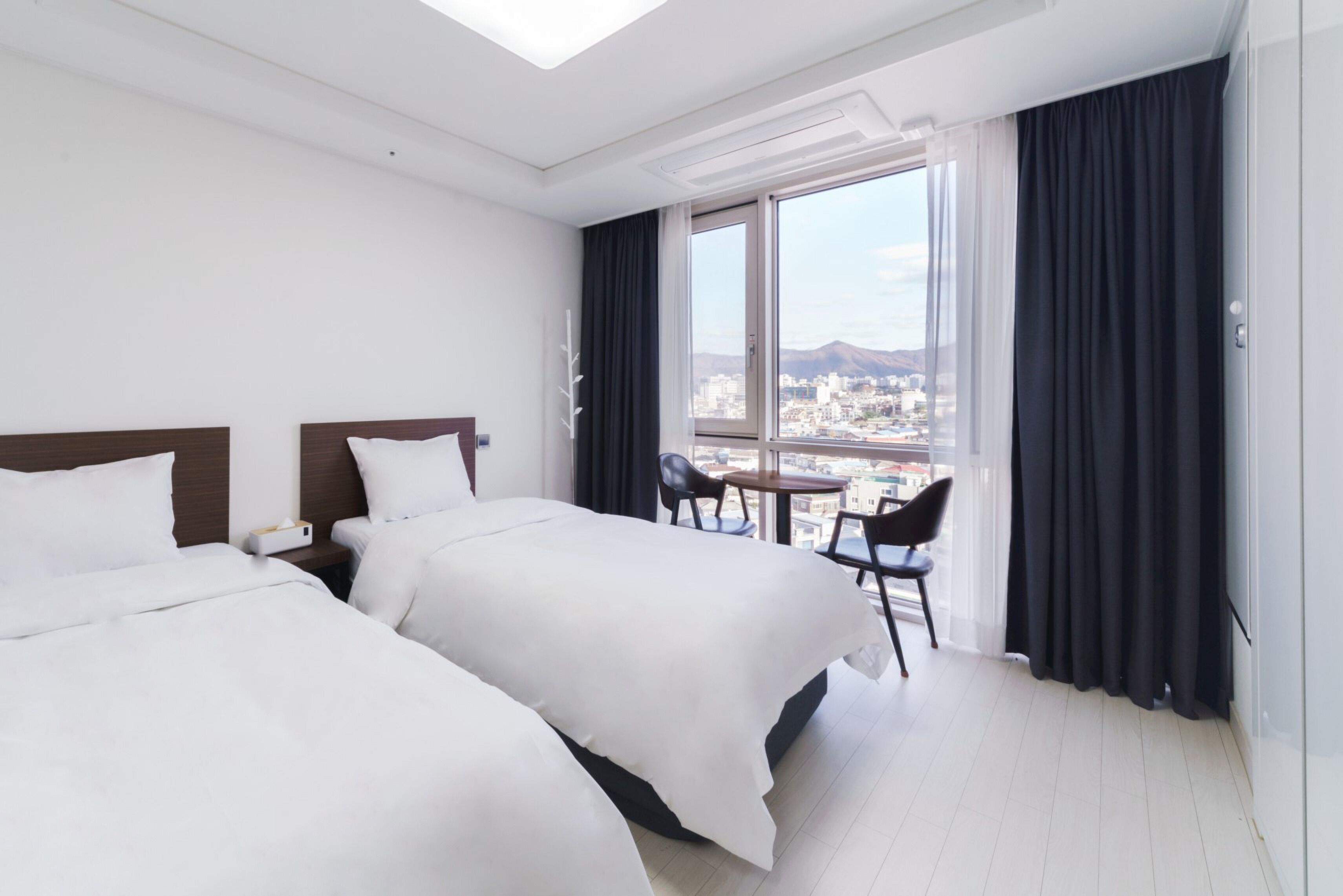A hotel room with two beds, a small table, and a chair.