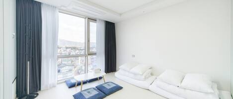 Una sala de estar moderna con un sofá blanco, cojines azules, una mesita y un ventanal con vistas a la ciudad.