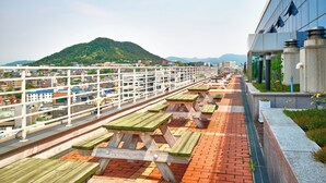 A rooftop terrace with picnic tables and a view of a cityscape and mountains. - The Venezia Suite Hotel (Chuncheon)