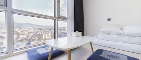 Una habitación de hotel moderna con un ventanal grande, una cama blanca y una mesita.