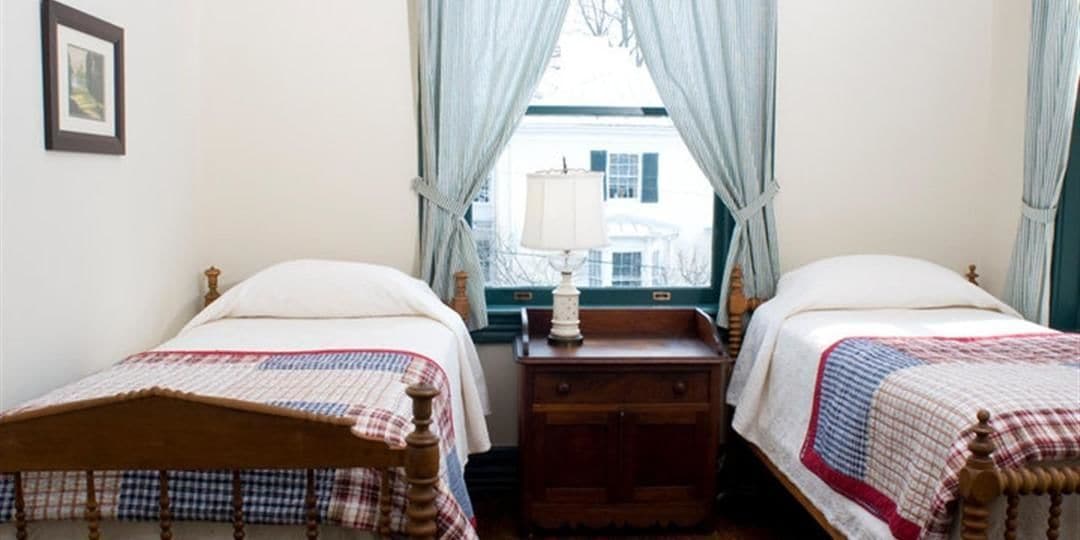 Ein Zimmer mit zwei Einzelbetten, einem Nachttisch mit Lampe und einem Fenster mit Vorhängen.