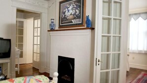 Una habitación con chimenea, un televisor sobre un mueble bajo, una puerta que da a otra habitación y un cuadro enmarcado sobre la chimenea.